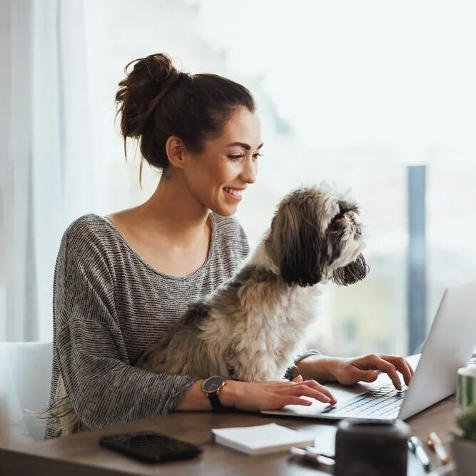 A woman at a laptop with a small dog